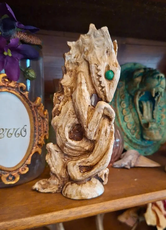 Front view of the Dagon Idol resin sculpture with a weathered antique bone finish and green eyes, displayed on a wooden shelf.