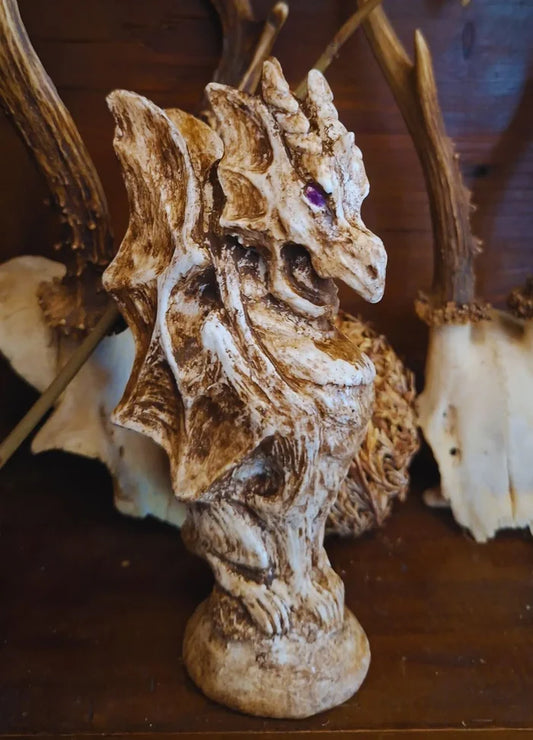 Three-quarters view of the handmade Gargoyle Dragon resin statue with a weathered antique bone finish and purple eyes, displayed on a wooden shelf.